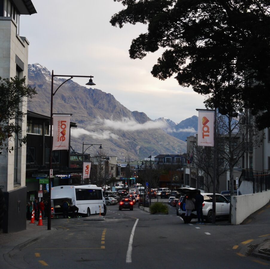 A downtown view of Queenstown, New Zealand with its iconicly massive mountain range in the backdrop.