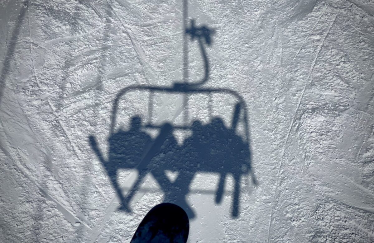 A shadow on the snow of skiers and snowboarders from a ski lift.