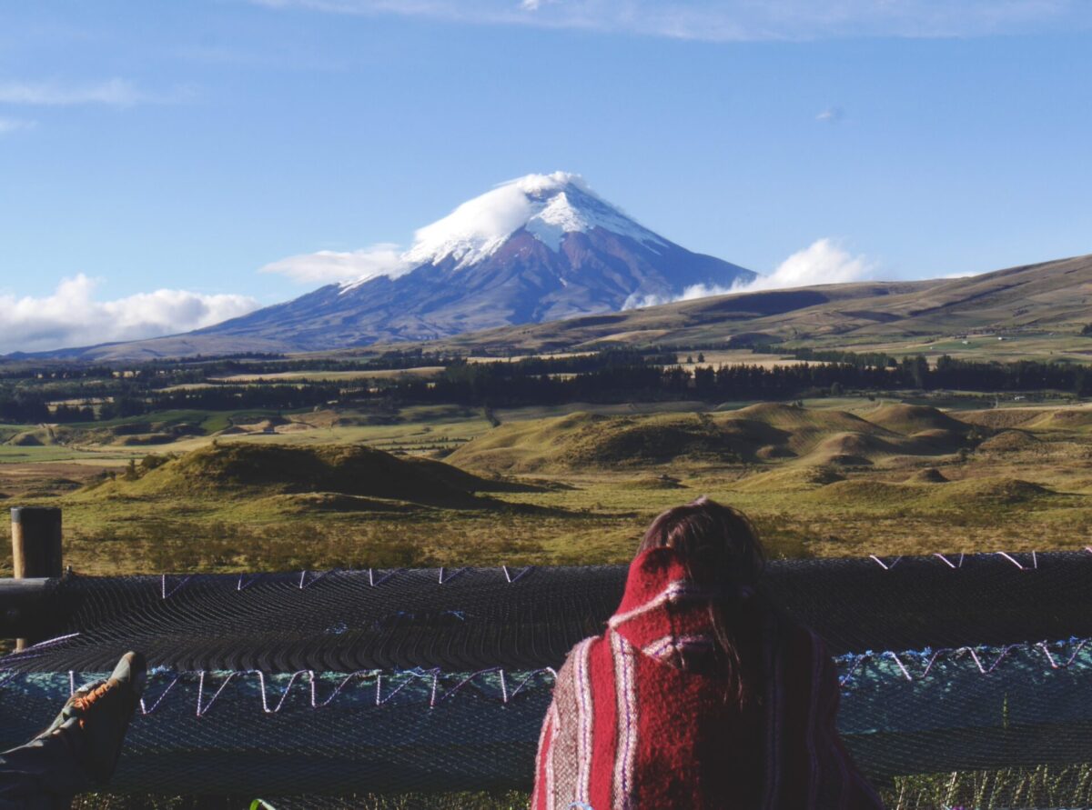 A woman sitting on a hammock in Ecuador while looking out at the huge Cotopaxi Volcano.