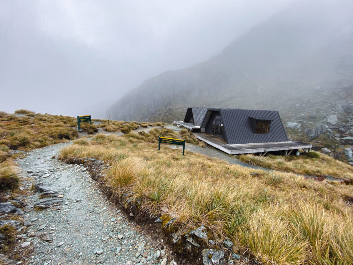 The Harris Saddle shelter on the Routeburn Track, surrounded by clouds and tussock grasses.