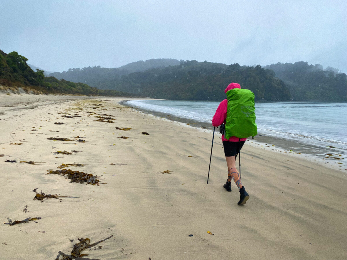 A hiker walks along a rainy beach on the Rakiura Track, Stewart Island, NZ.