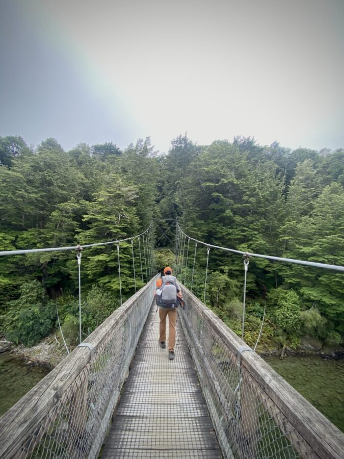 A hiker crossing a bridge on the Kepler Track in New Zealand.