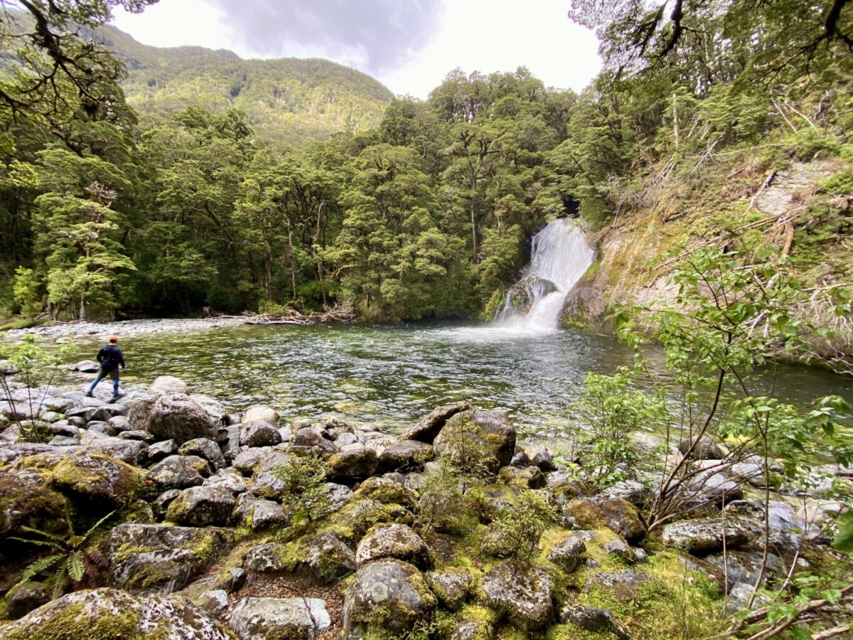 A hiker standing in front of the Iris Burn Falls near the Kepler Track in Fiordland National Park.