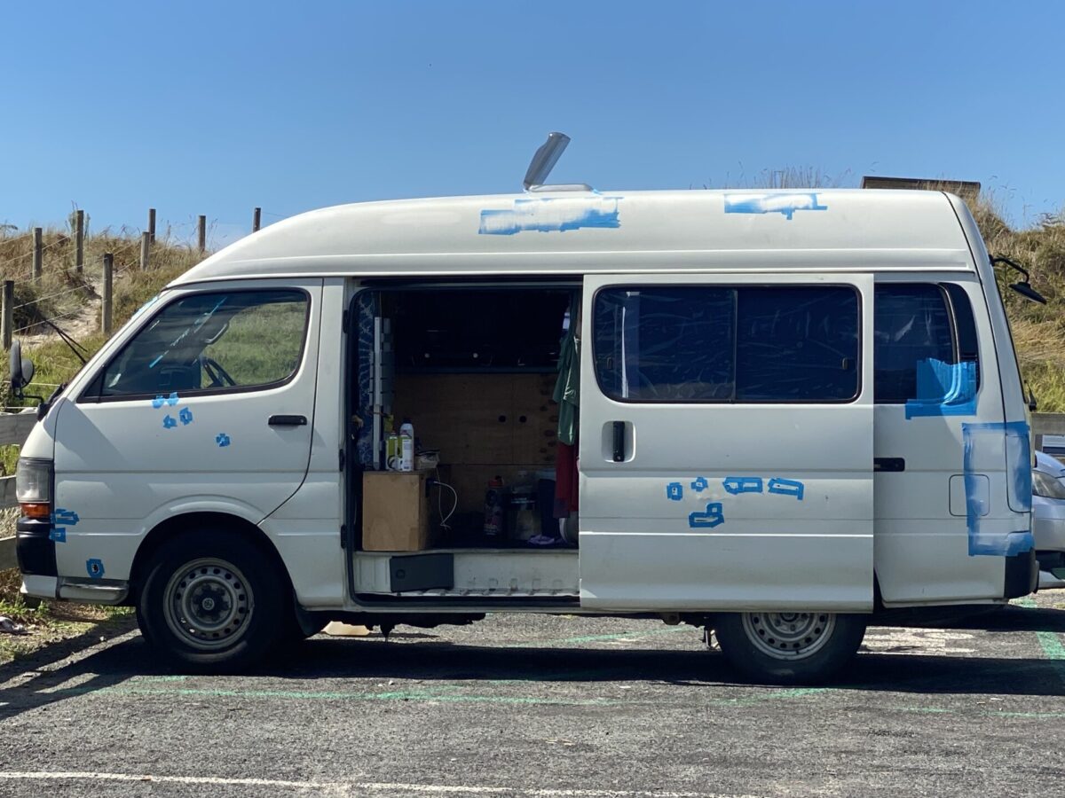 A converted van taped up on the outside for a DIY rust treatment and paint job.