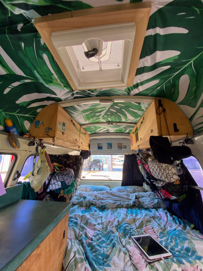 An inside of a converted van showing some counter space, overhead storage, a bed, and a roof vent.