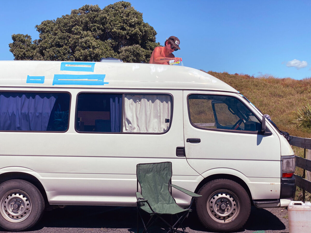 A converted van getting a DIY rust makeover in a New Zealand parking lot.
