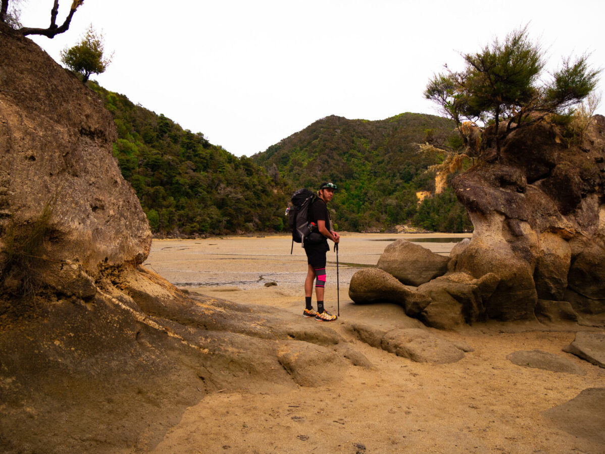 A backpacker crossing the Torrent Bay Inlet on New Zealand's Abel Tasman Track.