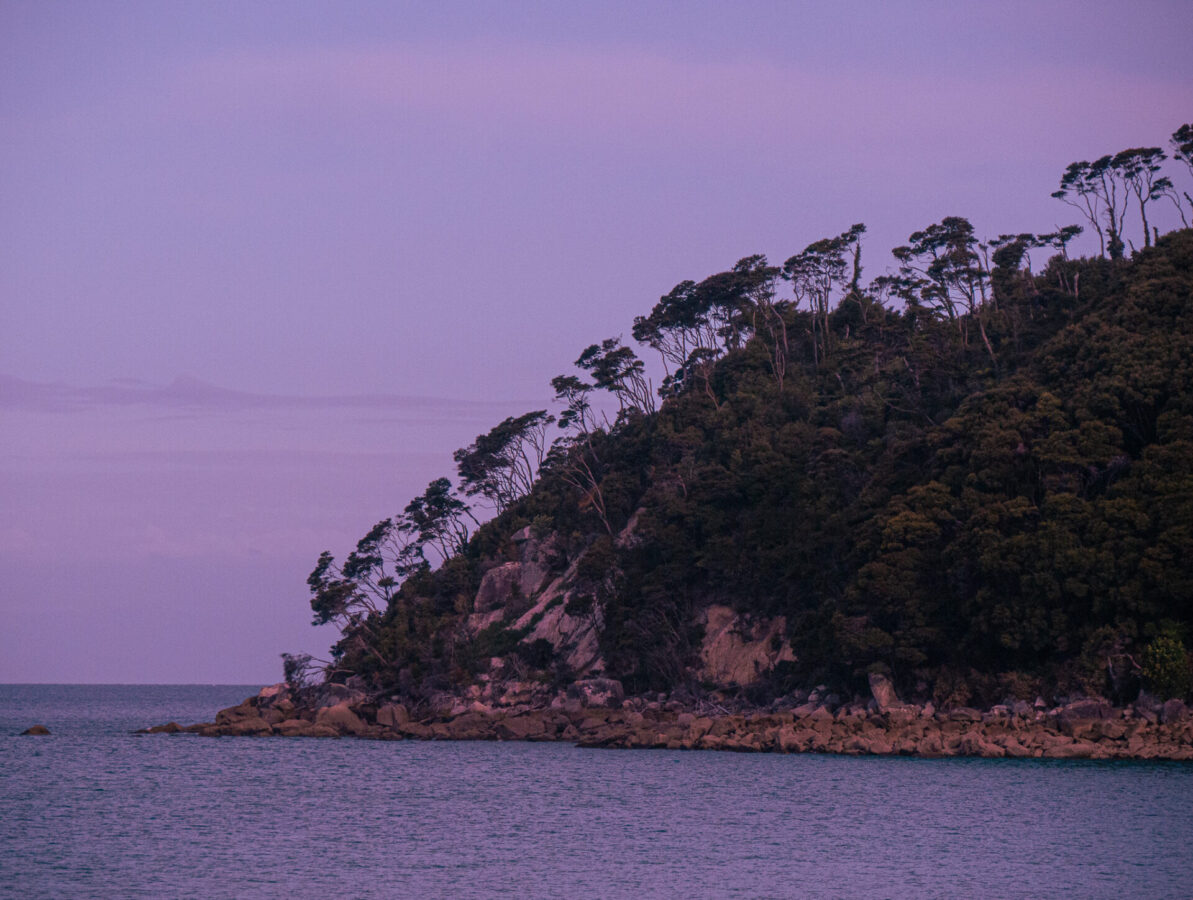 A sunset view of the nearby rocky cliffs from Bark Bay along the Abel Tasman Track in New Zealand.