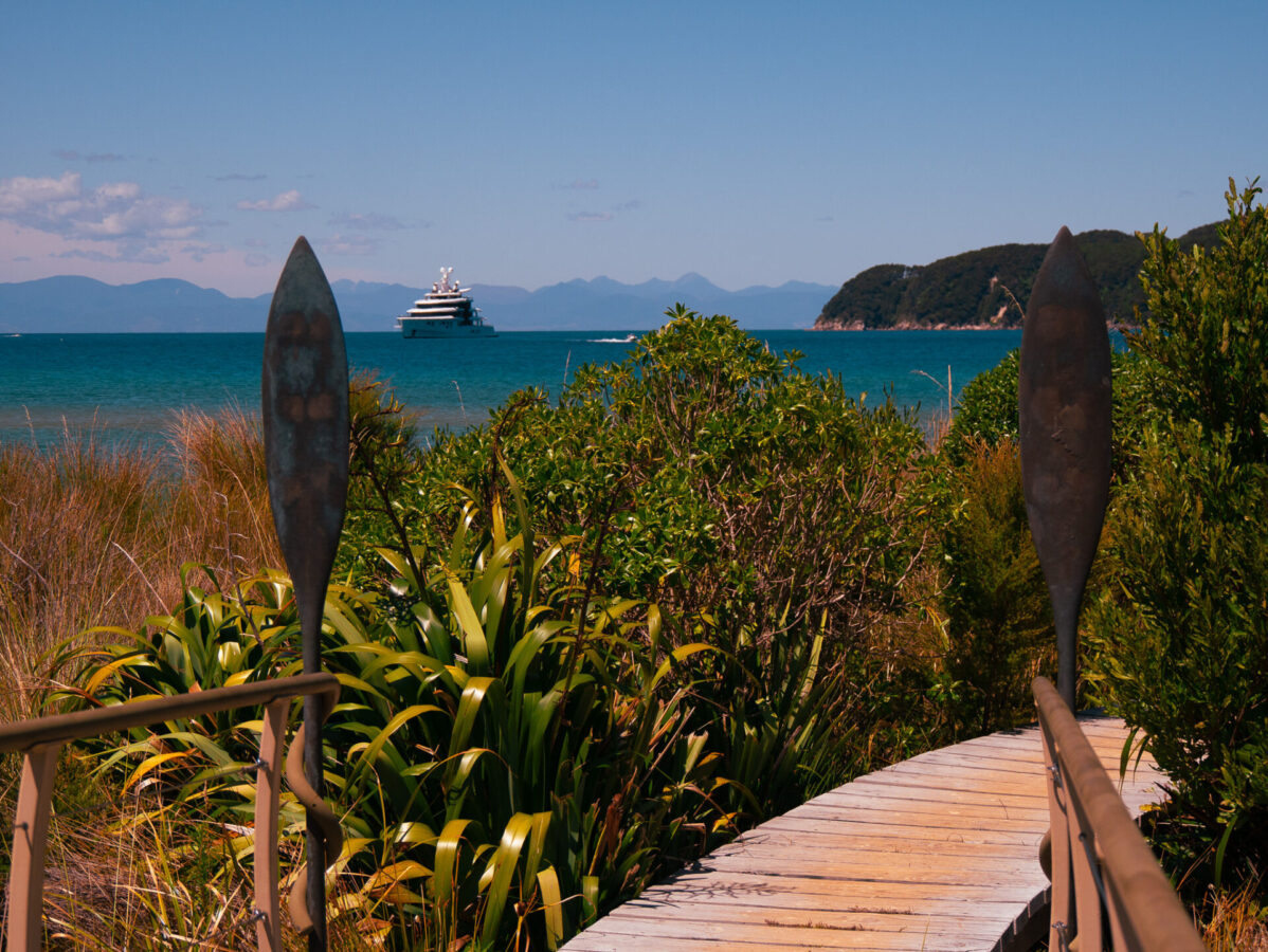A bridge at Onetahuti Beach on New Zealand's Abel Tasman Track, with a large yacht and Tonga Island in the background.
