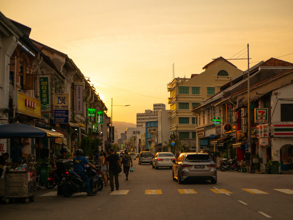 A view of a busy street in George Town, Malaysia during a yellow and orange sunset.