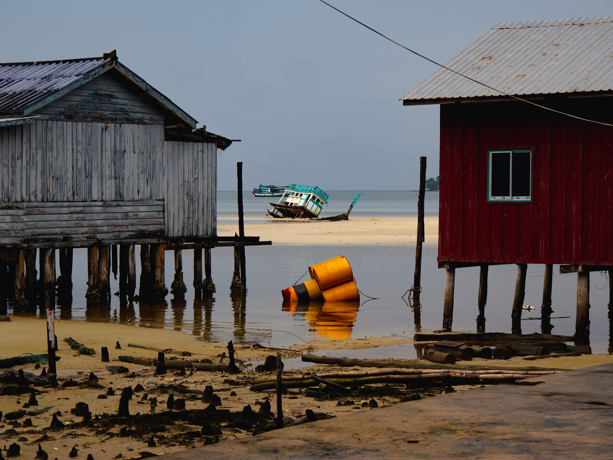 A partially sunken ship and colorful wooden buildings on stilts at the shoreline of Koh Rong, Cambodia's Prek Svay fishing village.