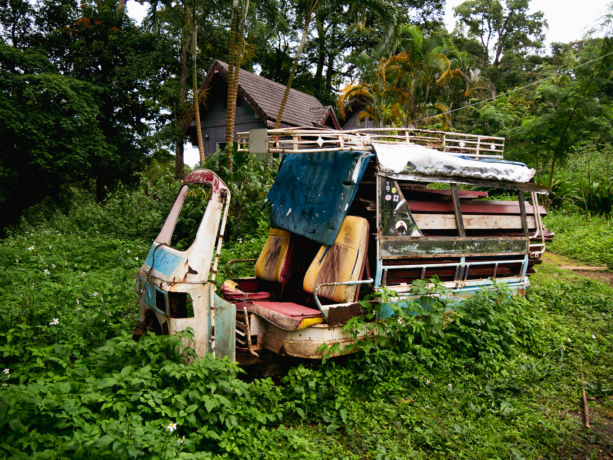 An old rusty tuk tuk tangled in weeds at an abandoned waterfall resort on Laos' Bolaven Plateau.