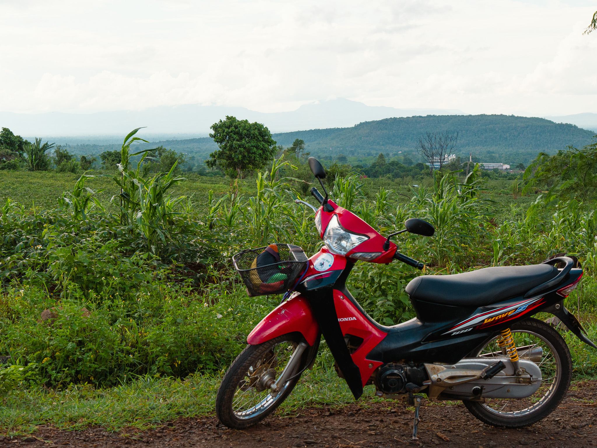 A red and black semiautomatic motorbike "posing" in front of a scenic view of the Bolaven Plateau in Laos.